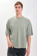 Camiseta verde de corte amplio y recto, con estampado de texto circular en la espalda.