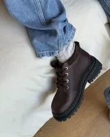 Borcego de cuero color gris con cordones color naranja, suela track negra de goma y detalle de gamuza en la parte superior del tobillo.