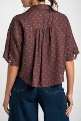 Blusa color crudo con estampado de lunares marrones, cuello camisero, cierre frontal con botones y mangas cortas holgadas.