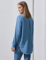 Camisa celeste de tencel, marca Hester & Orchand. Tiene cuello con solapa, escote en V, abertura central con botones, bolsillo aplicado en el frente y ruedo desflecado.