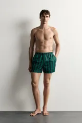 Short de baño confeccionado en tejido técnico, con diseño de rayas verticales en color verde y negro. Cuenta con cintura elástica ajustable con cordón, bolsillos laterales y bolsillo trasero con vivo, además de forro interior.