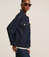 Campera trucker de jeans azul oscuro, corte amplio, con cuello clásico, cierre frontal con botones blancos, mangas largas y bolsillos delanteros con solapa.