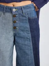 Pantalón ancho de mujer, estilo patchwork, combinando paneles de tela en tonos beige claro, beige medio y marrón. Presenta cierre frontal de botones y costuras contrastantes en rojo.