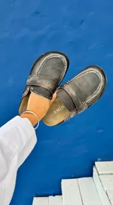 Zueco tipo mocasín marca Amén, confeccionado en cuero con acabado desgastado y costuras visibles en el borde. Presenta una plantilla ergonómica y diseño abierto en el talón.