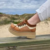 Zapatos de cuero estilo trekking en tonos marrones y beige, con plataforma alta y suela track. Presentan detalles de textura trenzada en los laterales y cordones finos.