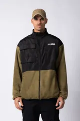 Campera de polar con recortes en tela técnica tipo sire en la parte superior frontal. Presenta cierre frontal completo, cuello alto y bolsillos funcionales en el pecho. Diseño bicolor en tonos verde oliva y negro con logo de la marca en el pecho.