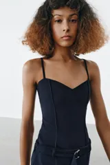 Top de escote en pico con tirantes finos ajustables. Presenta un diseño entallado con costuras verticales decorativas en el frente y bajo recto.