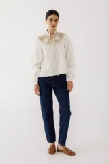 Blusa de lino color beige con cuello de crochet tejido y lazos frontales para anudar. Presenta mangas largas abullonadas con puños ajustados.