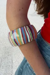 Pack de dos pulseras rígidas de resina, una fina con rayas horizontales multicolores y otra más ancha con rayas verticales multicolores.