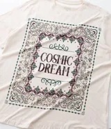 Remera de algodón color beige con cuello redondo, mangas cortas y corte holgado. Presenta un estampado frontal con la frase 'Cosmic Dream' rodeada por un diseño de estilo bandana.