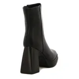 Bota corta de mujer color negro, con caña ajustada, punta cuadrada y cierre lateral. Presenta una plataforma delantera y un taco ancho y alto con textura de madera.