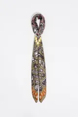 Charm para bolso con forma de pañuelo confeccionado en poliéster con estampado Ikatmix que combina motivos florales y abstractos en tonos verde oliva, malva, blanco y amarillo. Incluye un anillo metálico plateado en forma de corazón para sujetar a carteras o accesorios.