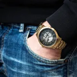 Reloj de pulsera con caja y malla de acero inoxidable en tono dorado. Presenta una esfera negra con diseño texturizado, manecillas luminiscentes y subesferas multifunción.