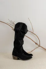 Bota estilo tejana de caña alta, confeccionada en gamuza, con taco cuadrado y diseño de costuras decorativas.