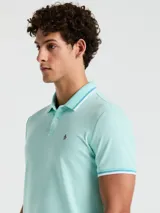 Polo de piqué color celeste con cuello clásico, tapeta de dos botones y logo bordado en el pecho. Detalles de ribete en cuello y mangas.