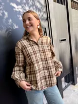 Camisa de corte holgado con estampado de cuadros escoceses en tonos beige y marrón. Presenta cuello clásico, cierre frontal con botones y mangas largas.