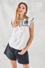 Blusa de color blanco con detalles bordados en negro, cuello redondo con cordones ajustables y mangas cortas con volados.