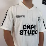 Chomba de tejido de punto color negro, con cuello polo y cierre frontal parcial. Presenta diseño de rayas verticales sutiles en el tejido, detalles de líneas blancas en los hombros y estampado frontal con texto y gráficos en color blanco.