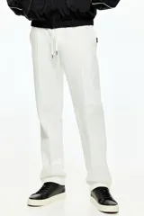 Pantalón tipo jogger de corte sastrero, color blanco, confeccionado en tejido de punto de peso medio. Presenta pliegue cosido frontal, cintura elástica con cordón de ajuste, bolsillos laterales y bolsillo trasero insertado.