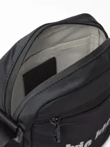 Bolso tipo reportero (crossbody bag) de color negro, confeccionado en poliéster resistente al agua. Presenta el logo de Calvin Klein en blanco con texto adicional que indica "West 39th Street" y "New York City". Tiene correa ajustable y múltiples compartimentos con cierre.