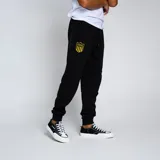 Pantalón de jogging negro con puños ajustados en los tobillos y cordón en la cintura. Presenta un escudo bordado en amarillo y negro en la pierna izquierda.