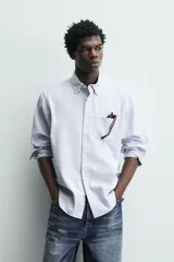 Camisa de corte regular fit confeccionada en tejido de algodón con diseño de rayas verticales. Presenta cuello abotonado, manga larga con puños abotonados, bolsillo plastrón en el pecho y cierre frontal con botones.