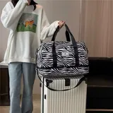 Bolso deportivo de viaje marca Zuomanni, con estampado animal print de leopardo en blanco y negro. Cuenta con doble asa de mano, correa de hombro ajustable y extraíble, y un compartimento inferior independiente con cierre.