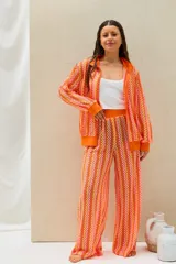 Conjunto de dos piezas tejido a crochet con diseño de ondas en tonos naranja, rosado y amarillo, compuesto por una camisa de manga larga y un pantalón largo de corte recto.