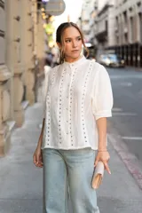 Blusa blanca con detalles bordados en toda la superficie, cuello levemente subido y botones al frente.