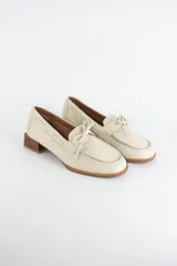Mocasín tipo náutico de cuero color crema, con cordones decorativos en el empeine y taco cuadrado bajo símil madera.
