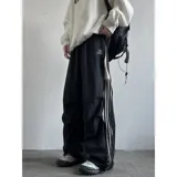 Pantalón deportivo negro de corte muy ancho (baggy) con cierre completo impermeable en los laterales. Presenta tres franjas blancas verticales en el lateral exterior de cada pierna. Posee reguladores en tobillos y cintura.