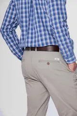 Pantalón de gabardina color marrón claro, corte slim fit, con bolsillos laterales y traseros. Se ajusta a la cintura con cinturón de cuero marrón.