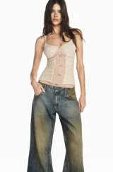 Musculosa de estilo corset confeccionada en tul beige con aplicaciones de encaje floral y cierre frontal con botones pequeños. Presenta breteles finos y un diseño semitransparente con frunces centrales.