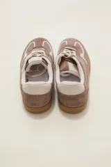 Zapatilla urbana de gamuza color marrón con detalles en beige, cordones claros y suela de goma tipo caramelo.