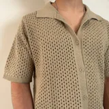 Camisa de tejido de punto calado en color beige, con cuello polo, cierre frontal de botones y mangas cortas.
