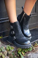 Bota corta negra de cuero con paneles de gamuza, cierre lateral con cremallera y tres hebillas decorativas.