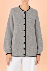 Cardigan de punto grueso en tono gris jaspeado, con cuello redondo y cierre frontal de botones. Presenta detalles de terminación en color negro con borde festoneado en el cuello, puños y ruedo, y mangas largas con puños ajustados.
