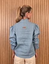 Blusa rosada de algodón con delicados bordados florales blancos, escote en V con cuello elevado y volados, y mangas largas con puños acampanados.