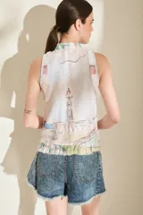 Top sin mangas de color blanco con estampado multicolor y detalles de volados desflecados, cuello mao y cierre frontal con botones.
