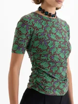 Top de punto color verde con estampado de dragones en tonos marrones y violetas. Tiene escote redondo, mangas cortas y frunces laterales que realzan la silueta.