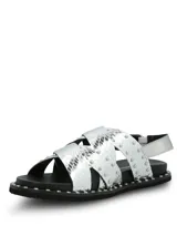 Sandalias planas de cuero plateado con textura efecto piel de serpiente y tachas metálicas aplicadas en las tiras cruzadas y en el borde de la suela. Cuentan con tira trasera con hebilla de ajuste.