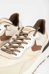 Zapatillas deportivas color crema con detalles en beige, negro y blanco.