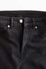 Jean de denim elástico color negro, de tiro alto, con cierre de botón y piernas acampanadas. Cuenta con bolsillos decorativos delanteros y bolsillos traseros.