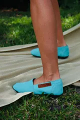 Alpargatas de lona color turquesa con suela plana de goma y detalle de etiqueta de cuero marrón con el logo grabado en el lateral.