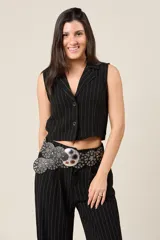 Cinturón ancho de ecocuero negro con múltiples apliques metálicos circulares tipo ojal y hebilla grande con diseño grabado.