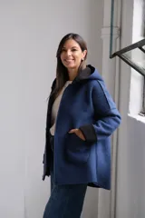 Tapado de paño azul con capucha, diseño de corte holgado y largo a la cadera. Presenta detalles en color negro en el interior, bordes y puños, con bolsillos frontales amplios y cierre frontal.