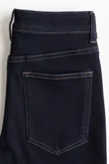 Jean de cinco bolsillos en denim oscuro, con leve elasticidad. Corte ajustado de tiro alto, ceñido desde la cintura hasta las piernas extraajustadas.