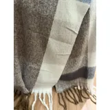 Bufanda rectangular de tejido grueso con diseño de cuadros en tonos azul, naranja, gris y beige, terminada con flecos en los extremos.