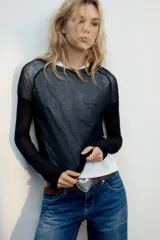 Jersey de punto semitransparente color gris claro, con cuello redondo y manga larga.