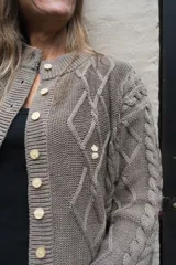 Saco tejido de punto con diseño de ochos y trenzas, color azul marino. Presenta cierre frontal con botones en contraste de color turquesa y un delicado bordado a mano en el pecho.